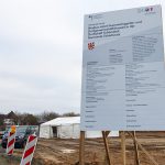 Gigantisch wirkt die Tafel mit der Baubeschreibung neben dem vergleichsweise winzigen Zelt für die Gäste der Grundsteinlegung
