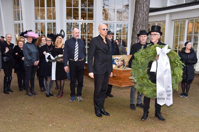 Der Sarg ist gefüllt mit Gemälden, der Kranz wird in Kürze niedergelegt: Trauerfeier für die Kunst vor der Timmendorfer Trinkkurhalle. © Susanne Dittmann